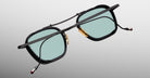 Jacques Marie Mage Baudelaire 2 black eyeglasses with gold nose pads and blue lenses, front view.
