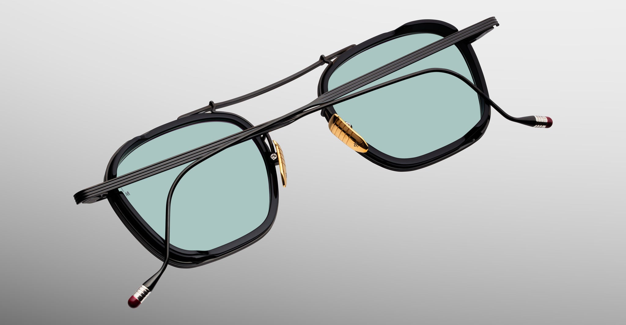 Jacques Marie Mage Baudelaire 2 black eyeglasses with gold nose pads and blue lenses, front view.