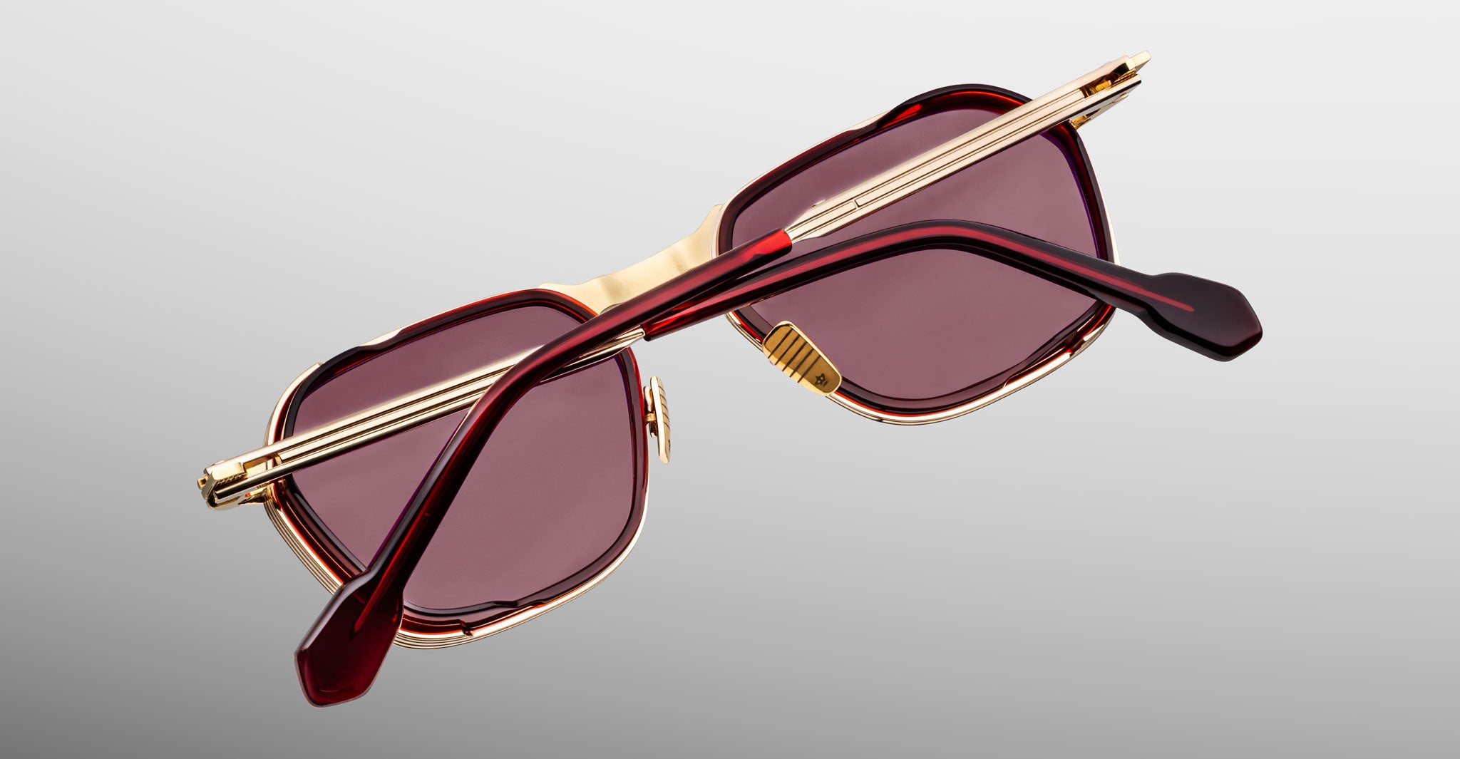 A pair of limited-edition Jacques Marie Mage Beckett sunglasses featuring rectangular gold frames, dark reddish lenses, and red and gold arms, displayed on a light gray gradient background.