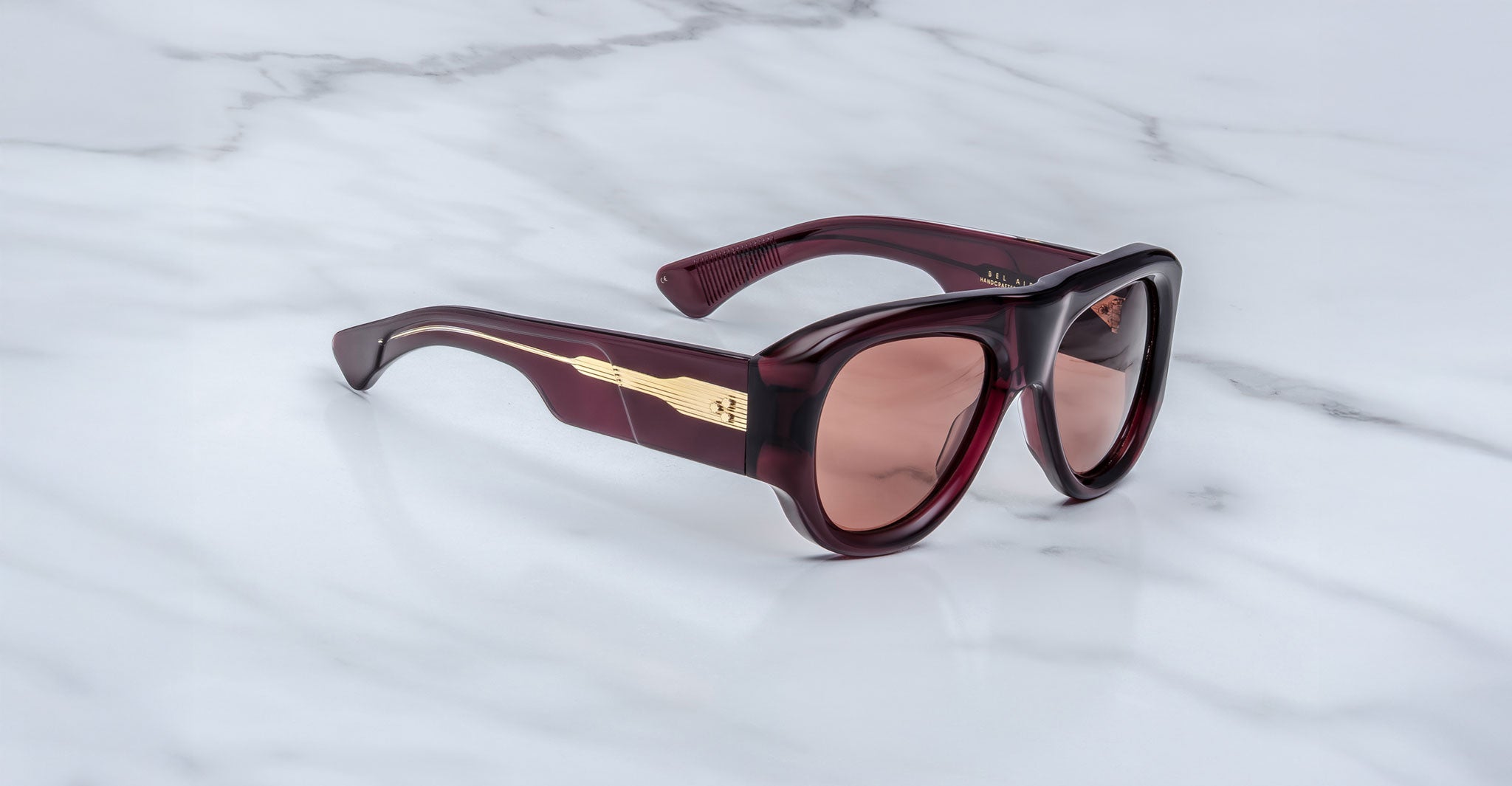 The Jacques Marie Mage Bel Air sunglasses, featuring oversized thick dark red translucent frames and brown tinted lenses, are displayed on a white marble surface.