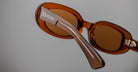Close-up of Jacques Marie Mage Besset brown oval sunglasses with translucent acetate arms, angled to show frame details.