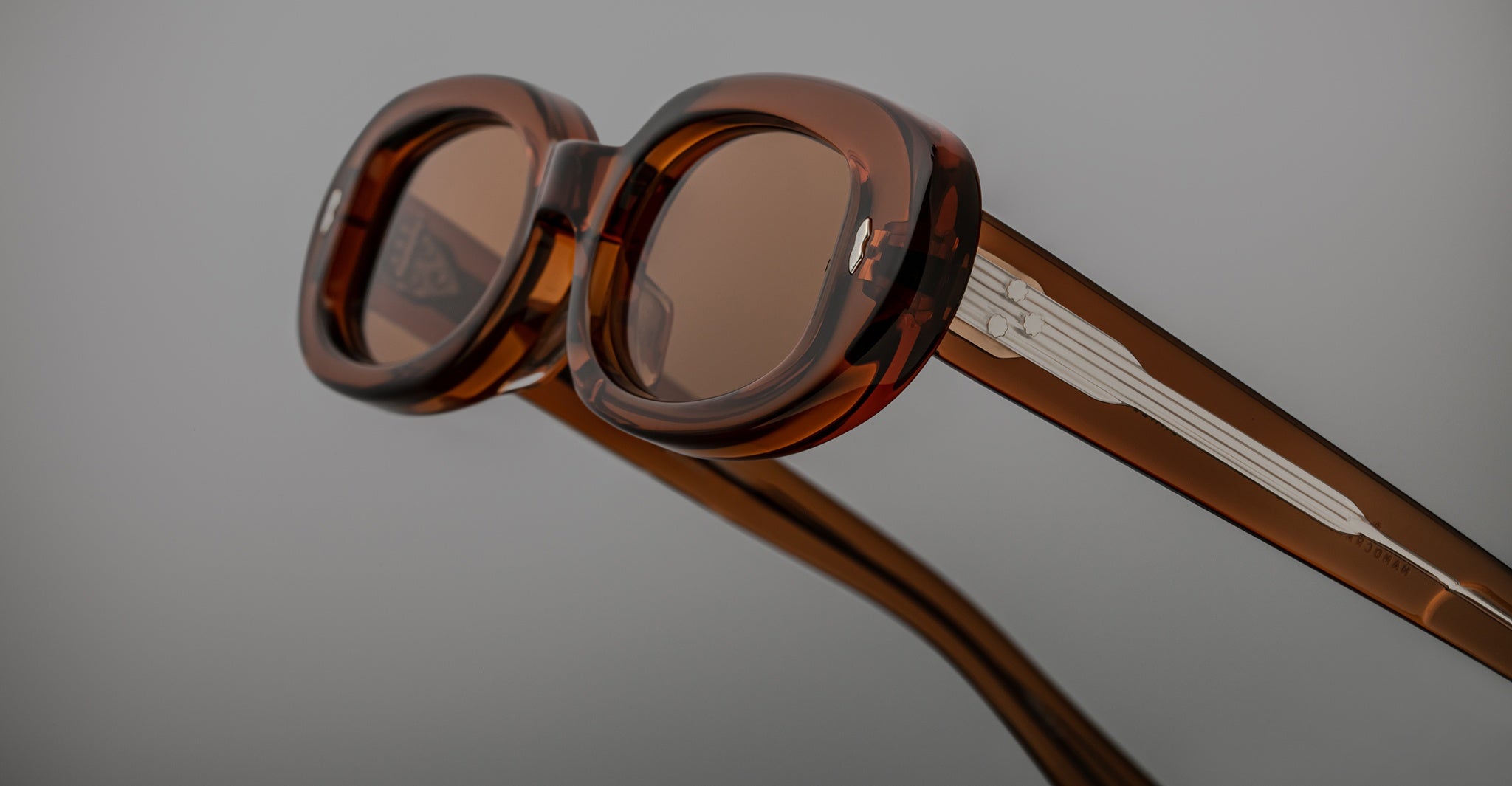 Close-up of Jacques Marie Mage Besset sunglasses, featuring brown translucent retro round frames and silver accents on the arms.