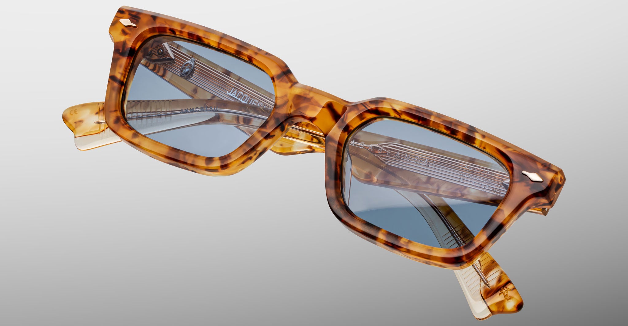 A pair of Jacques Marie Mage Casablanca rectangular tortoiseshell sunglasses with blue lenses is shown against a plain light gray background, with the arms folded.