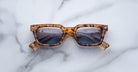 A pair of Jacques Marie Mage Casablanca rectangular tortoiseshell sunglasses with dark lenses laid flat on a white marble surface.