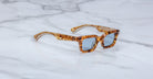 The Jacques Marie Mage Casablanca sunglasses feature thick, amber and brown tortoiseshell rectangular frames with blue-tinted lenses, displayed on a white marble surface.