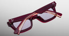 A pair of folded Jacques Marie Mage Casablanca rectangular eyeglasses with thick dark red translucent frames and silver dot accents on the temples, displayed on a light gray gradient background.