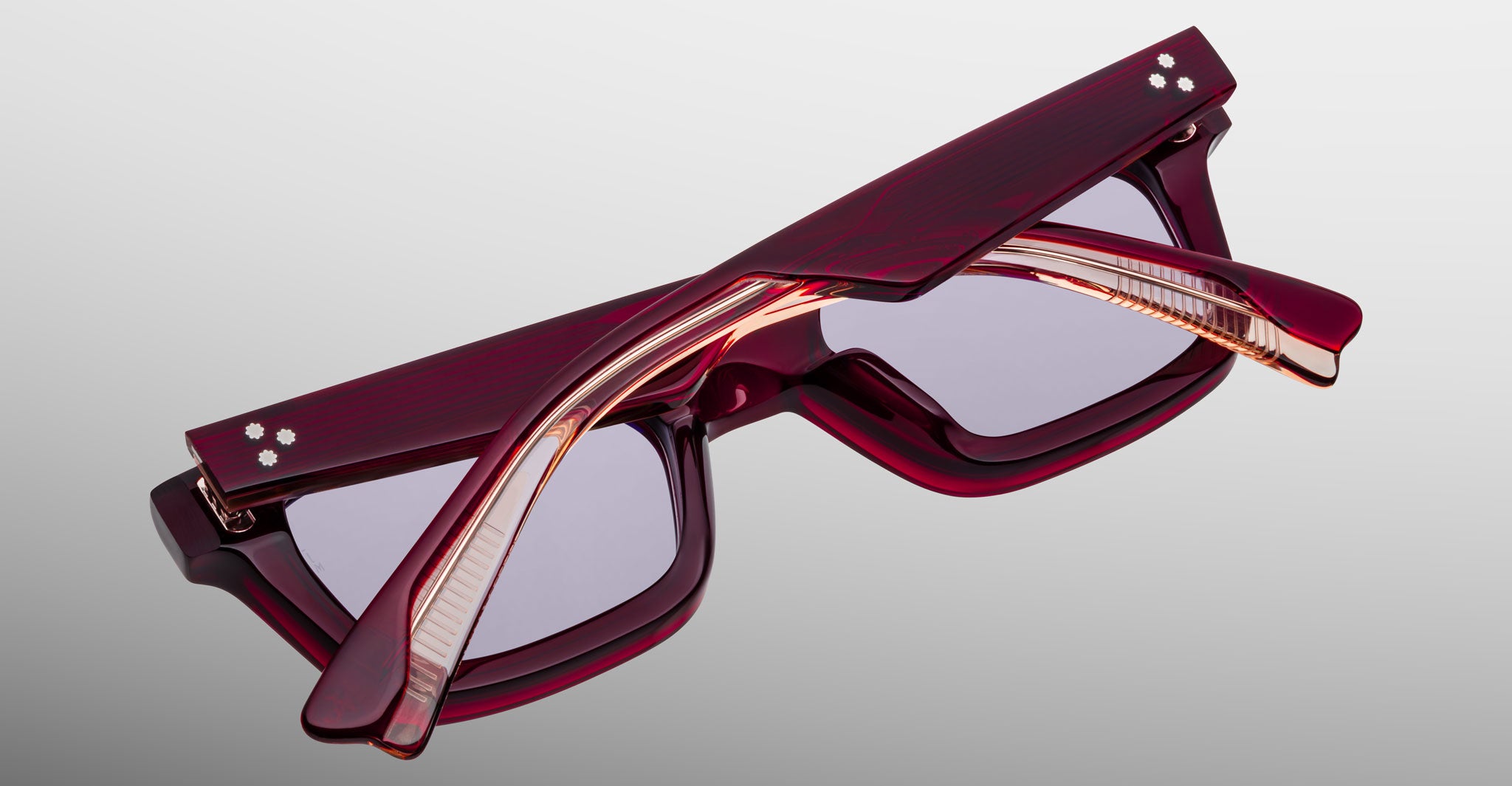 A pair of folded Jacques Marie Mage Casablanca rectangular eyeglasses with thick dark red translucent frames and silver dot accents on the temples, displayed on a light gray gradient background.
