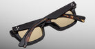 A pair of Jacques Marie Mage Casablanca sunglasses with black and tortoiseshell square frames, light brown lenses, and temples adorned with two small silver dots near the hinges, resting closed on a light gray background.