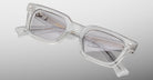 The Jacques Marie Mage Casablanca features clear acetate rectangular frames with light gray tinted lenses, visible hardware near the hinges, and gold text on the inner arm, shown against a gradient gray background.