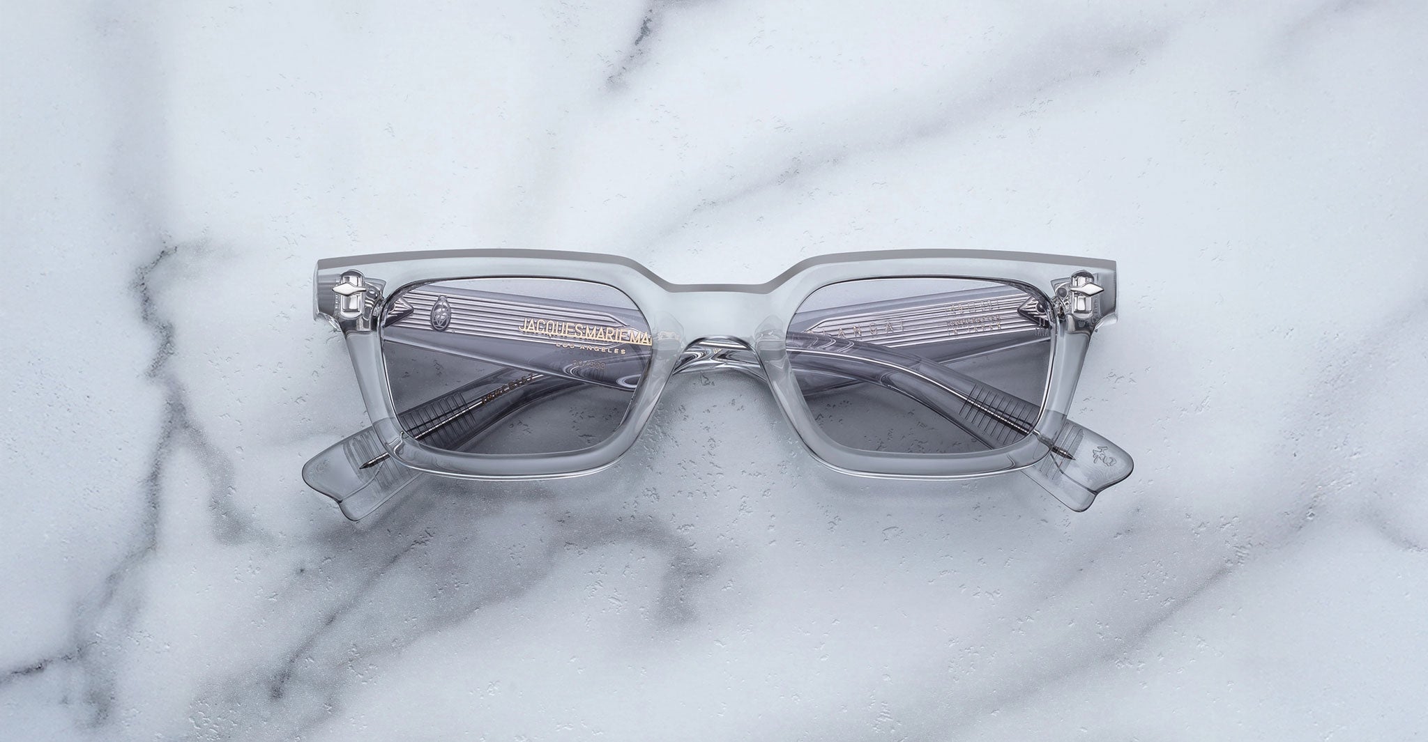 A pair of Jacques Marie Mage Casablanca rectangular sunglasses with thick translucent gray frames and tinted lenses rests on a white marble surface.