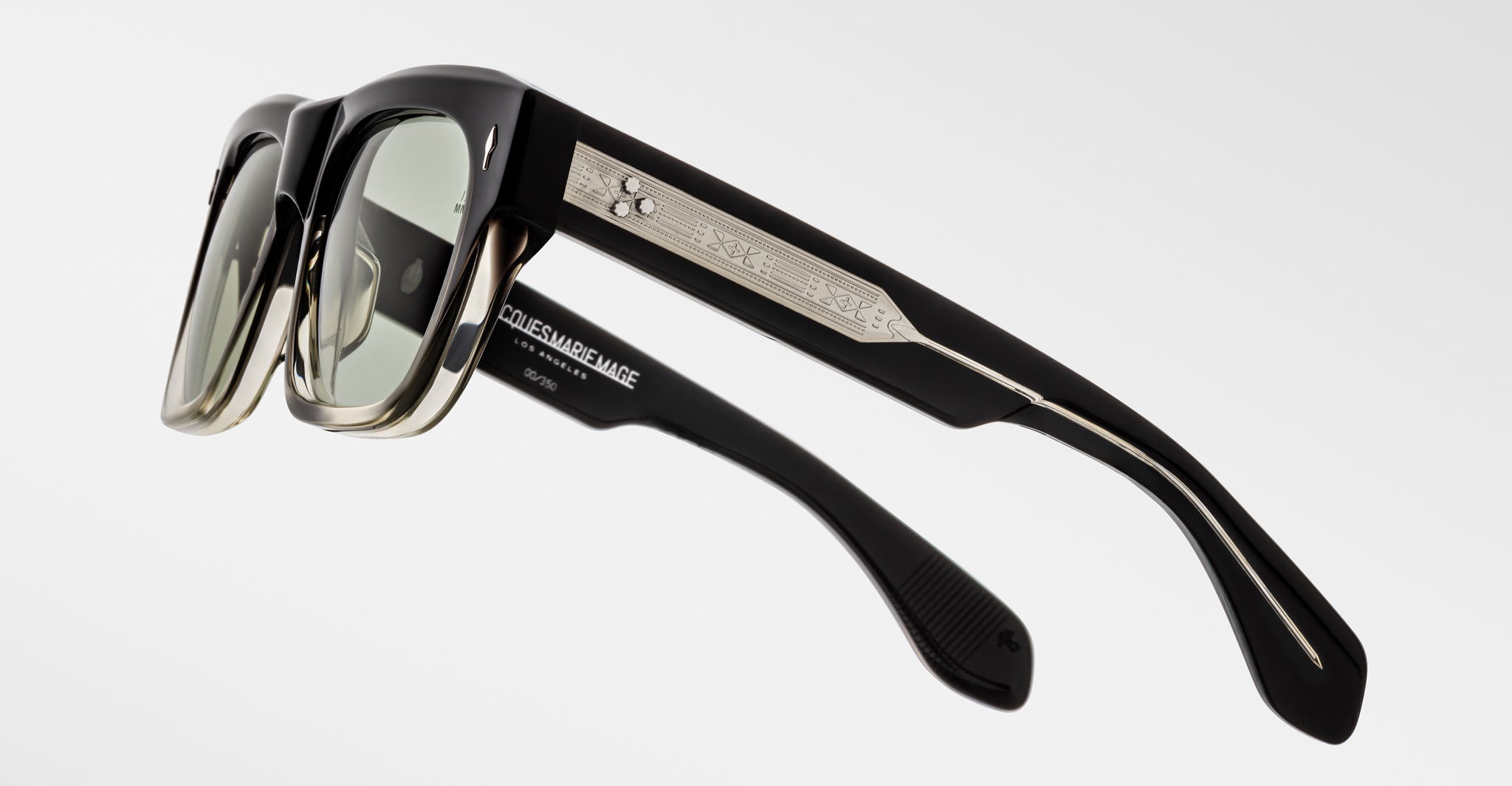 The Jacques Marie Mage Cash sunglasses feature black rectangular lenses, metallic silver detailing, and engraved patterns on the temples, displayed from a side angle against a plain white background.