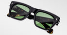 The Jacques Marie Mage Cash sunglasses feature black rectangular frames, green lenses, and tortoiseshell-detailed arms with branded and etched signatures on the inner sides, shown against a plain light background.