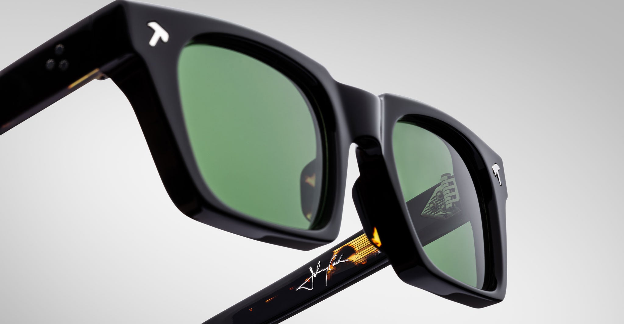 Close-up of Jacques Marie Mage Quentin sunglasses, featuring black frames, green lenses, and a white signature on the arm.
