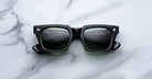Jacques Marie Mage Quentin sunglasses with thick frames shown from above, road reflection visible in lenses.