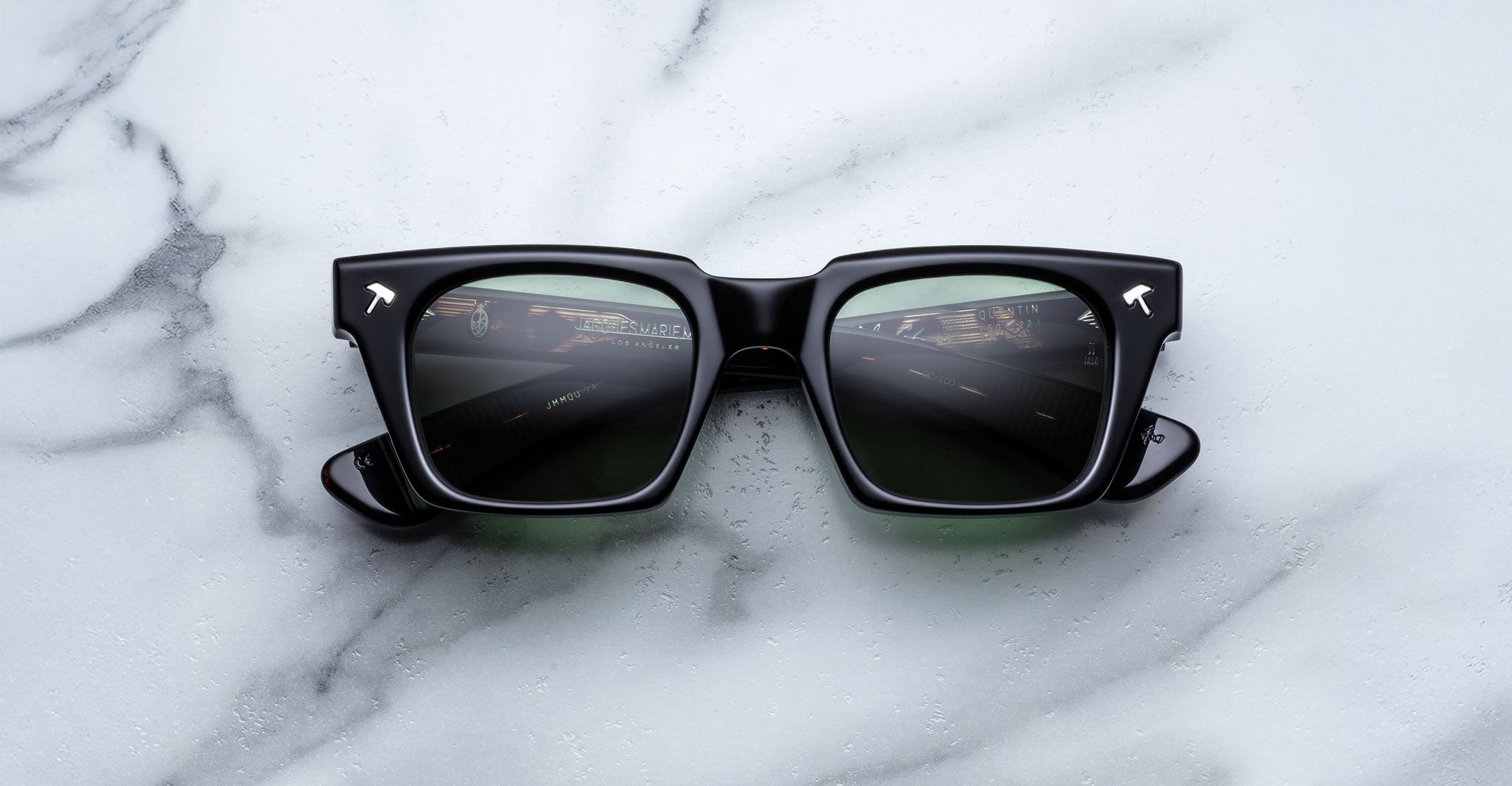 Jacques Marie Mage Quentin sunglasses with thick frames shown from above, road reflection visible in lenses.