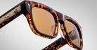 Close-up of Jacques Marie Mage Cash sunglasses with tortoiseshell frame and amber lenses, shown against a plain background. Features gold detailing on the arms plus visible branding and signatures inside the arms.