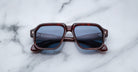Jacques Marie Mage Challenger sunglasses with square dark tortoiseshell frames and blue-tinted lenses rest on a white marble surface.