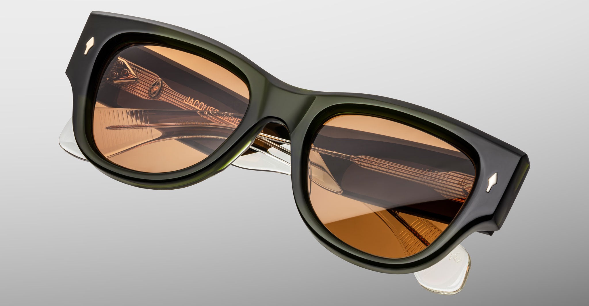 A close-up of Jacques Marie Mage Chelsea sunglasses featuring thick black frames and rectangular brown-tinted lenses, set against a plain light gray background.