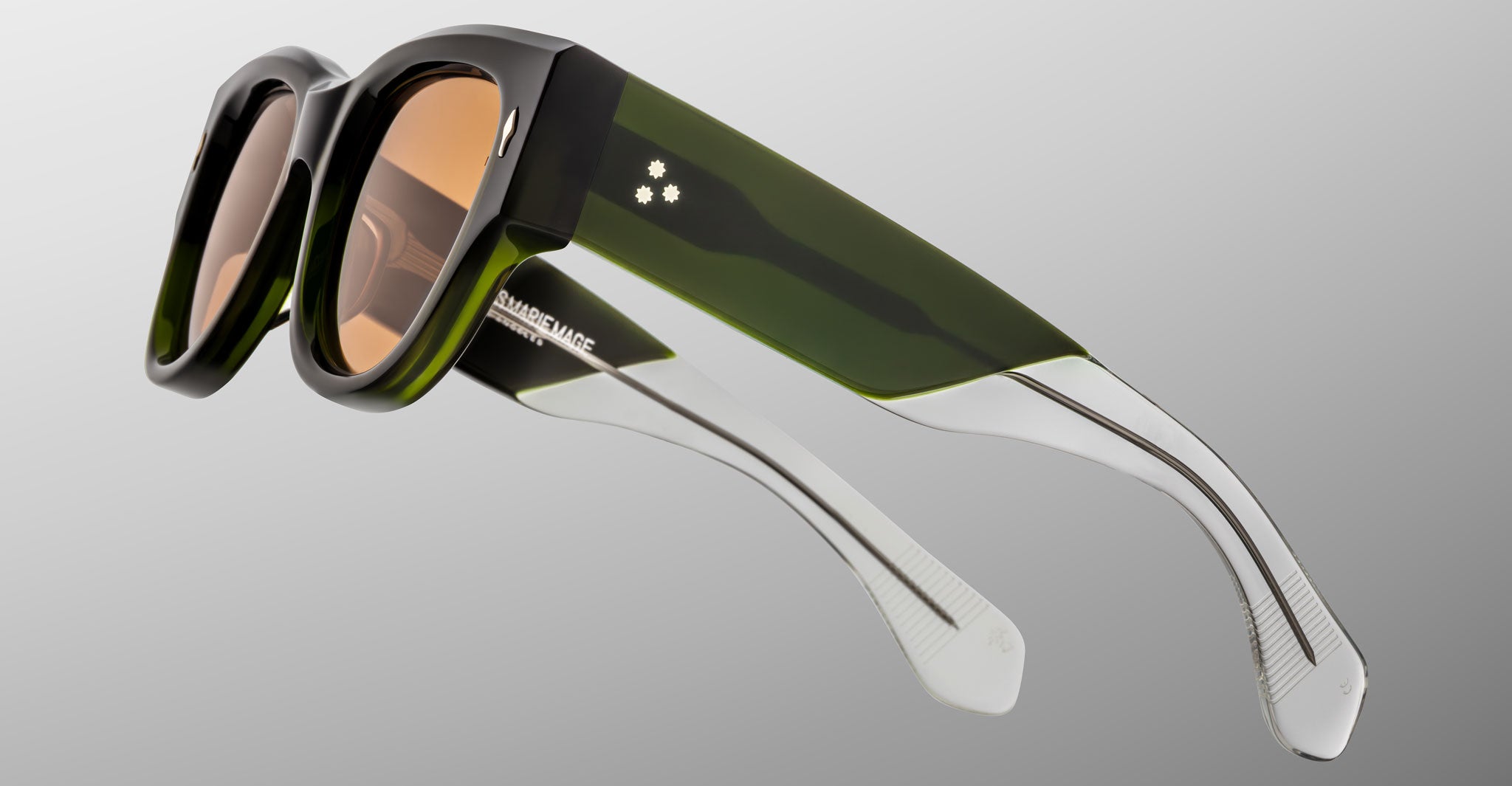The Jacques Marie Mage Chelsea sunglasses feature thick black and green frames with clear arms, brown-tinted lenses, and are displayed against a plain light gray background.