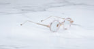 The Jacques Marie Mage Clark features round, clear frames with thin metal arms—midcentury-inspired optical glasses from Jacques Marie Mage—elegantly displayed on a white marble surface.