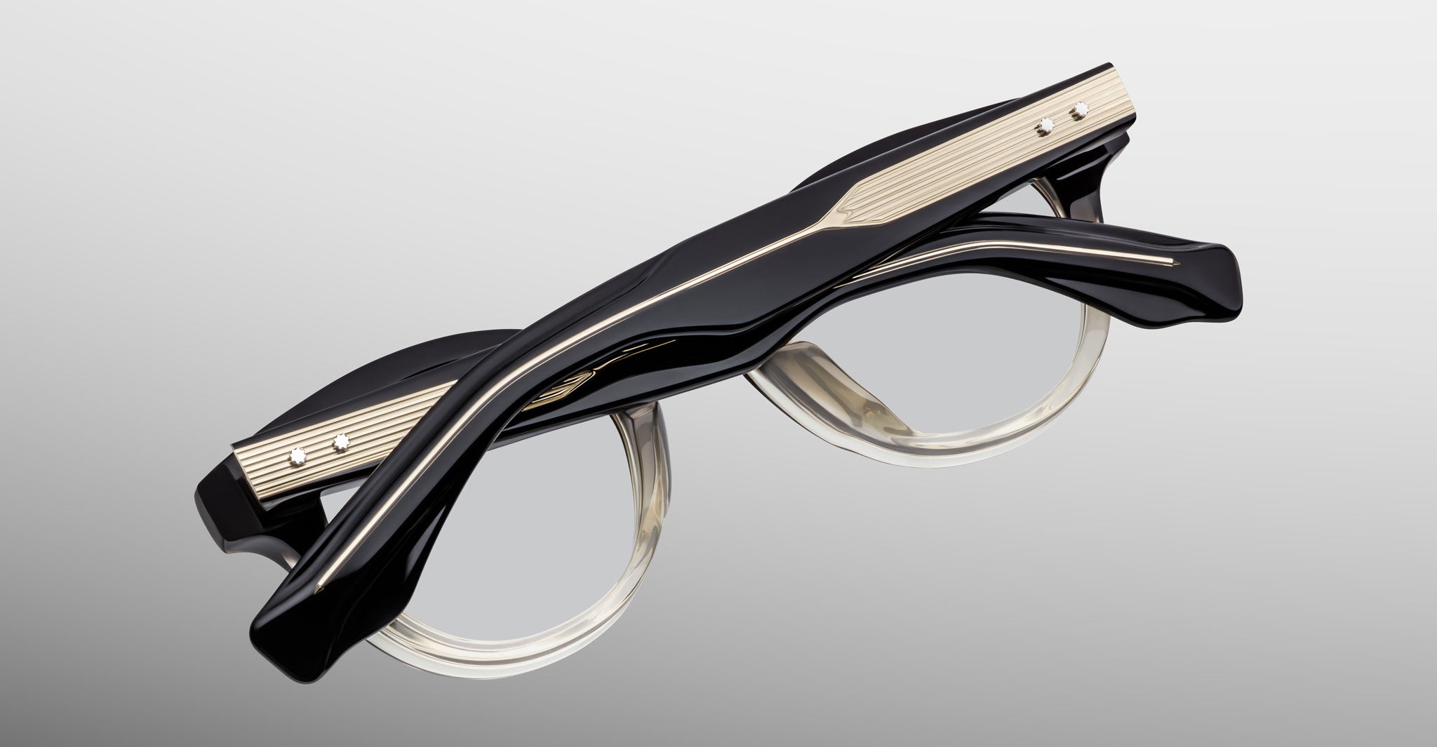 A pair of Jacques Marie Mage Clemens eyeglasses in black with thick, sculpted frames and gold accents on the temples, displayed against a light gray background.