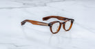 The Jacques Marie Mage Clemens are brown, round Wellington glasses with thick frames and metal-accented temples, displayed on a white marble surface.