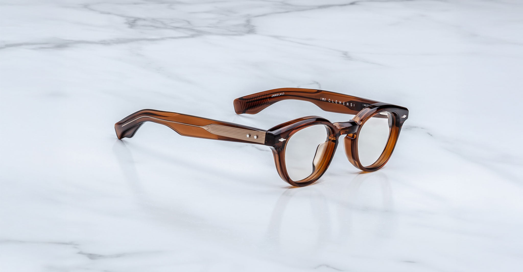 The Jacques Marie Mage Clemens are brown, round Wellington glasses with thick frames and metal-accented temples, displayed on a white marble surface.