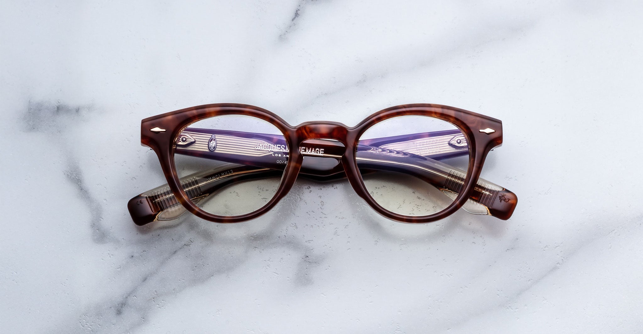 Jacques Marie Mage Clemens in Honeycomb round tortoiseshell eyeglasses with purple-tinted lenses, top-down view.