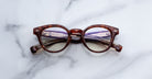 Jacques Marie Mage Clemens in Honeycomb round tortoiseshell eyeglasses with purple-tinted lenses, top-down view.