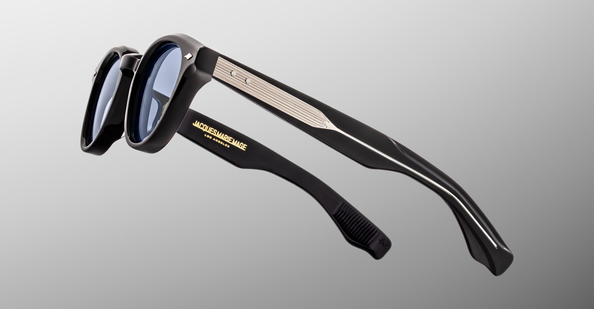 Jacques Marie Mage Clemens in Obscure sunglasses, black frame, blue lenses, silver accents, gold branding on inner temple, side view.