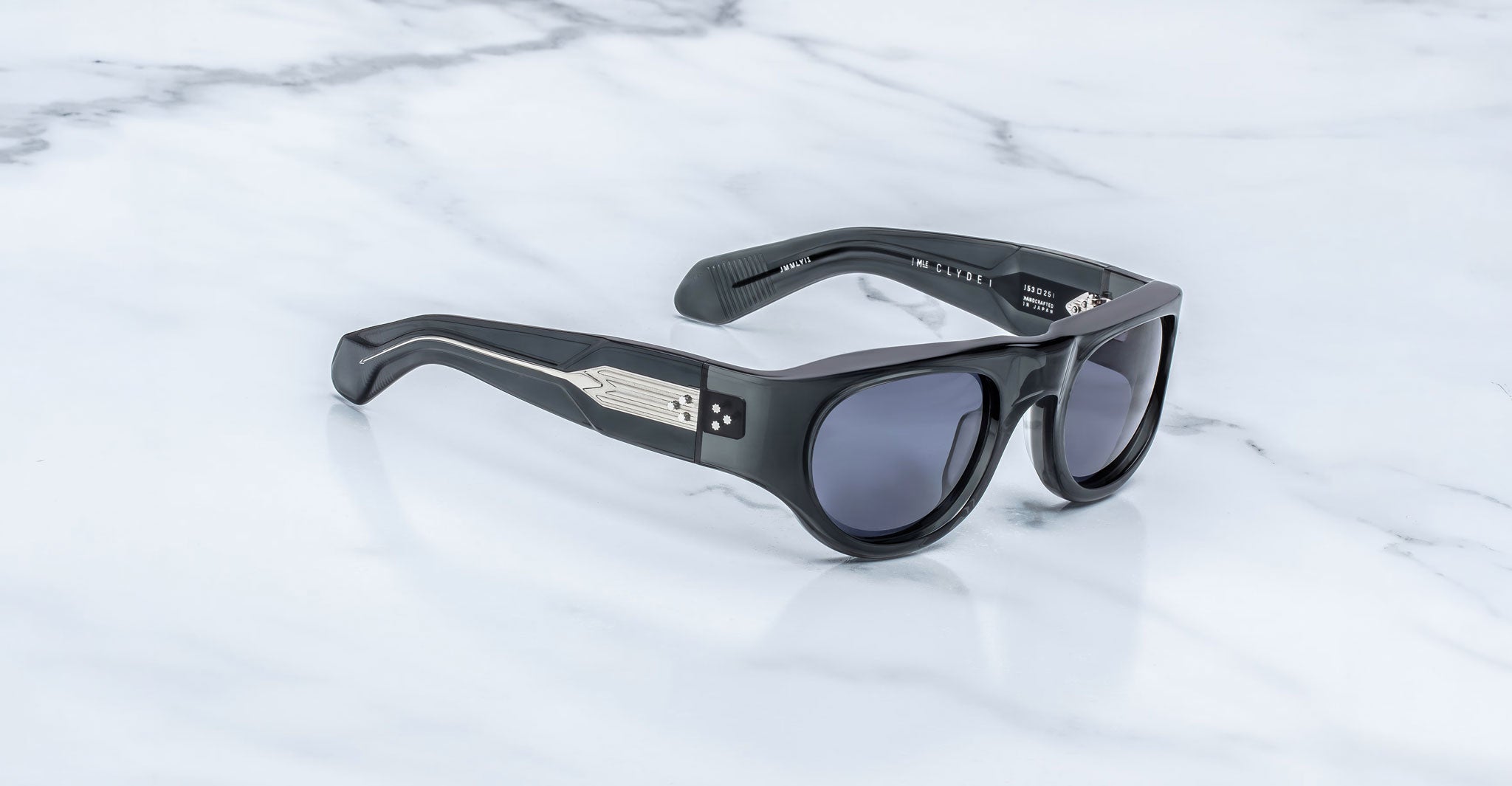 3/4 view of the Jacques Marie Mage Clyde 2.0 sunglass in Grisaille Black acetate, dark gray lenses, with a marble background