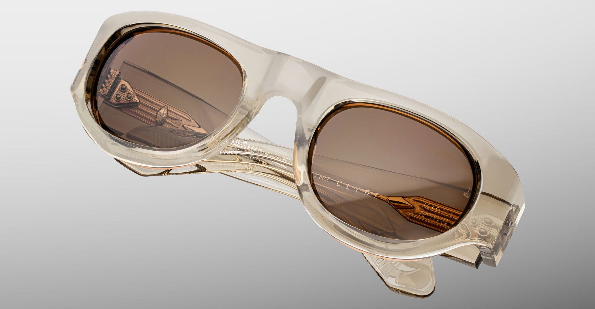 Detailed front view of the Jacques Marie Mage Clyde 2.0 sunglass in Marzipan translucent tan acetate with brown lenses on a light gray background
