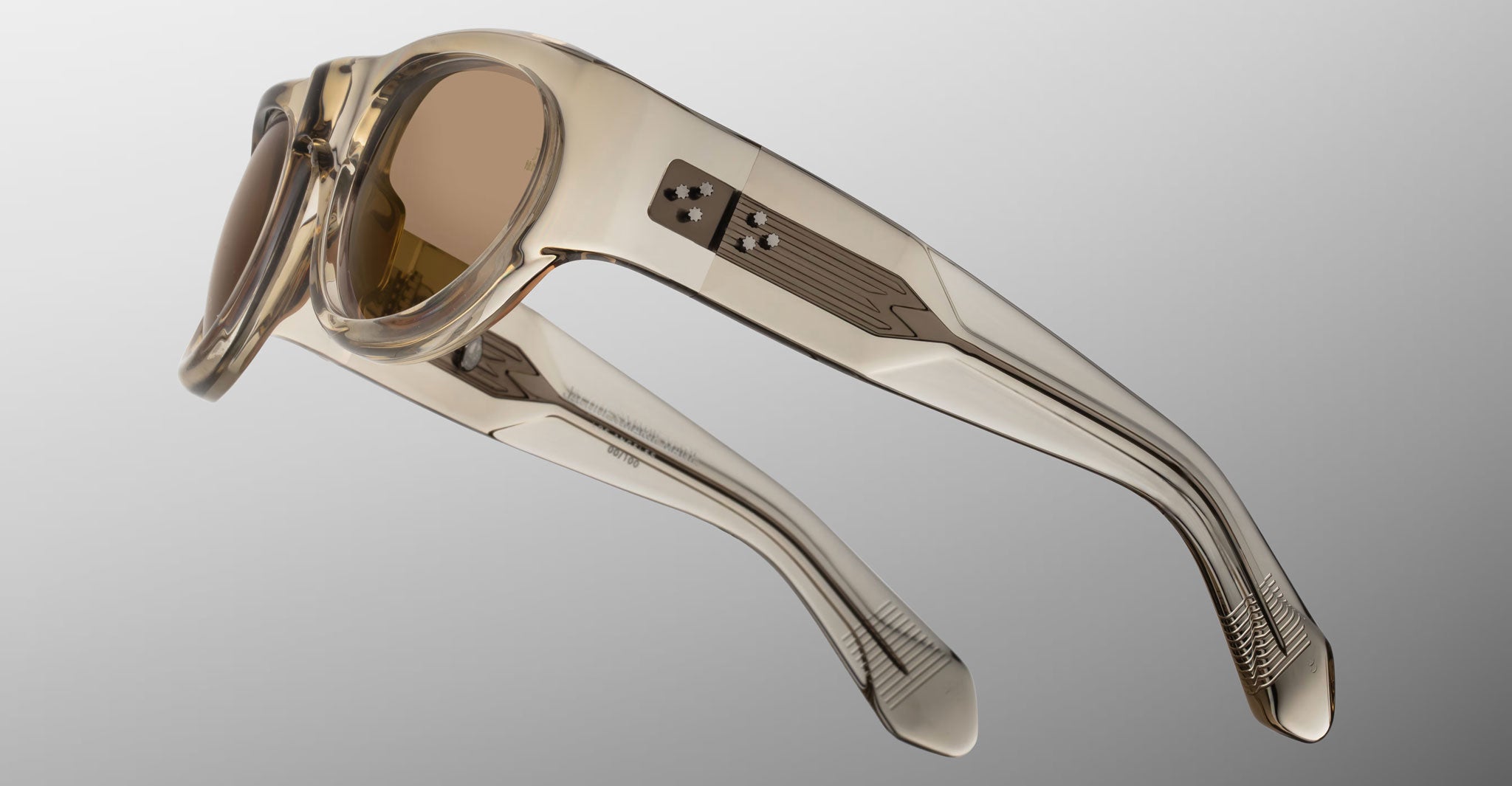 Detailed side view of the Jacques Marie Mage Clyde 2.0 sunglass in Marzipan translucent tan acetate with metal temple inner wirecore and brown lenses on a light gray background