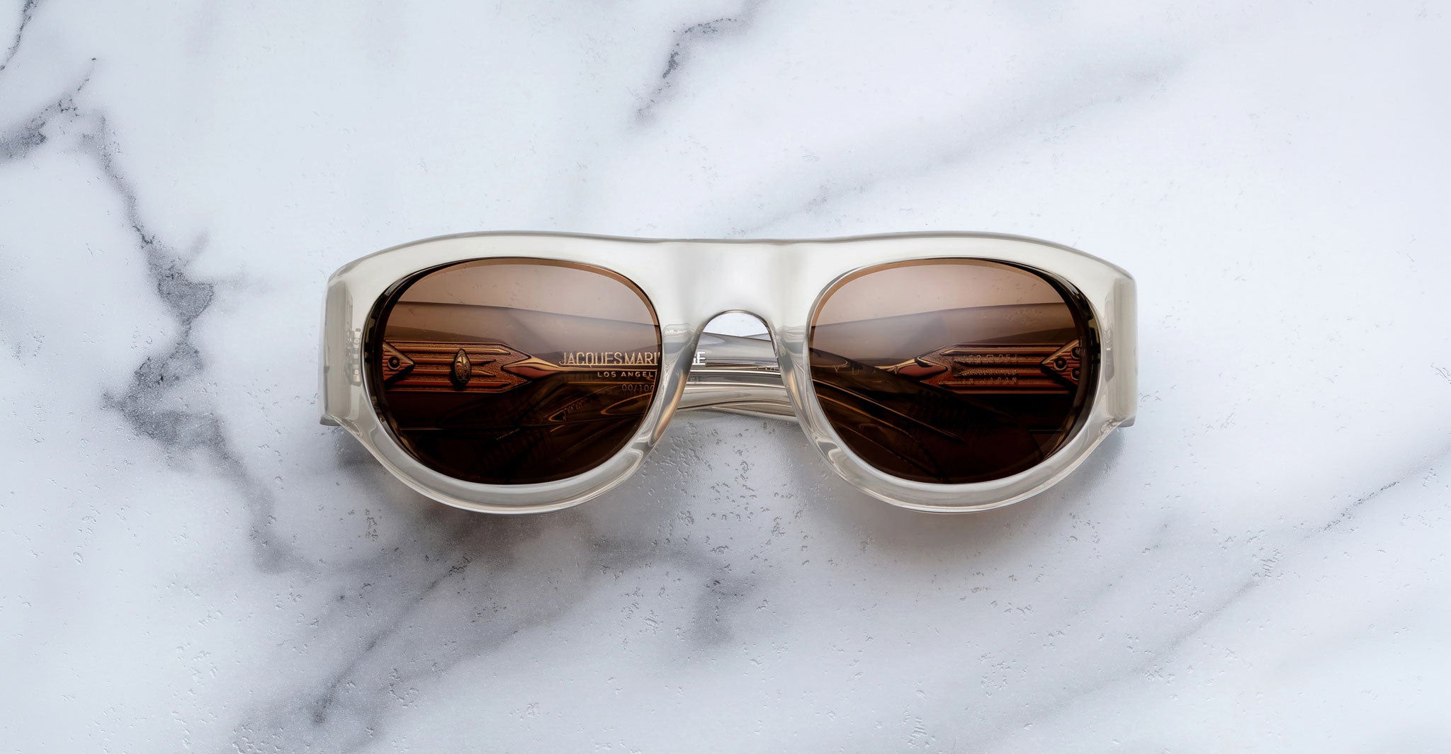 Front view of the Jacques Marie Mage Clyde 2.0 sunglass in Marzipan translucent tan acetate with brown lenses on a marble background