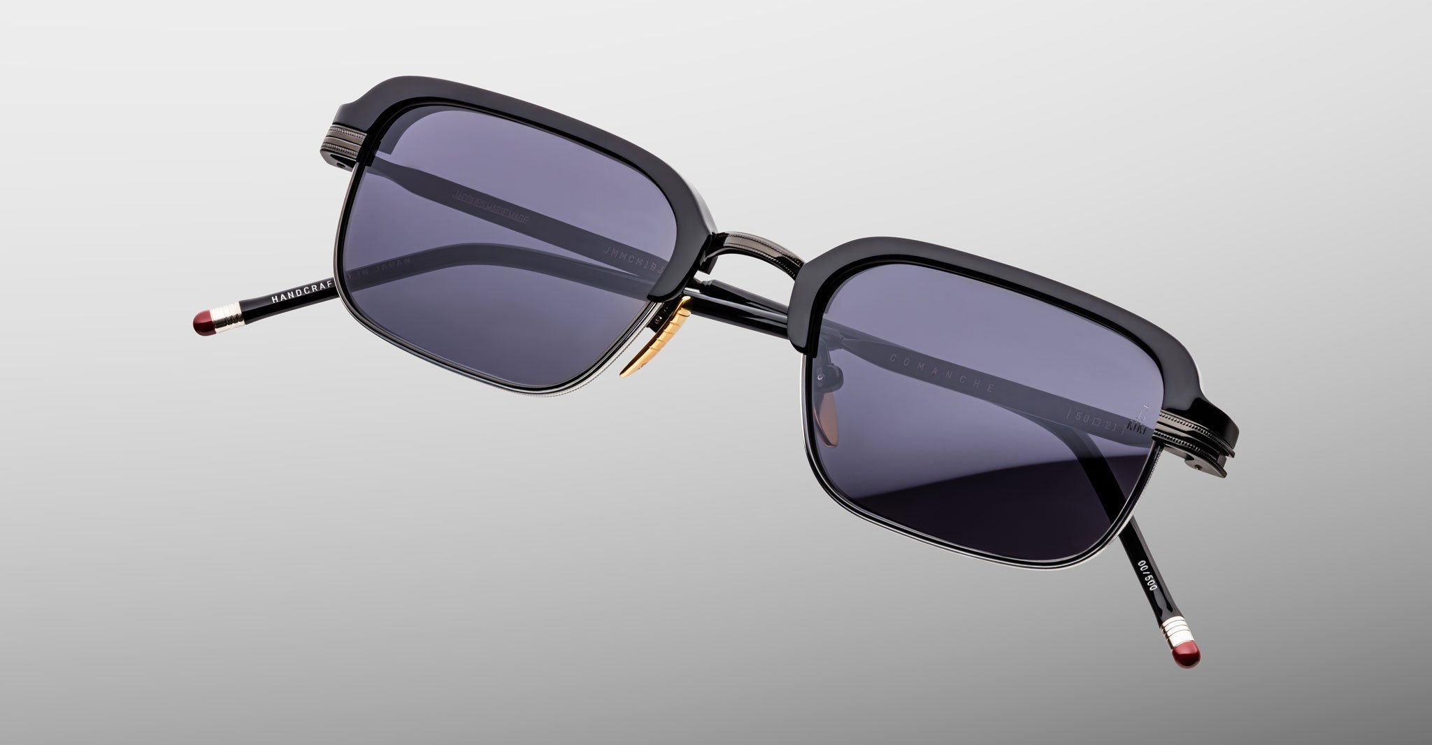 Jacques Marie Mage Comanche sunglasses: rectangular, black, handcrafted frames with dark lenses and gold nose pads, shown on a light gray background—a standout limited-edition piece from Jacques Marie Mage.