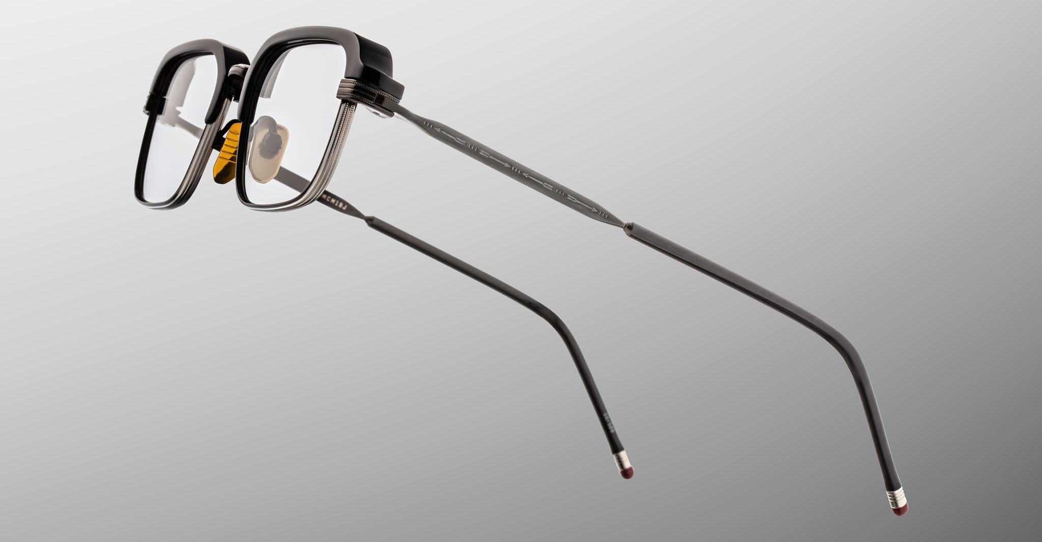 The Jacques Marie Mage Comanche eyeglasses feature black rectangular frames with thick rims and slim metal arms, suspended against a plain gray background, highlighting the expert craftsmanship of this limited-edition design by Jacques Marie Mage.