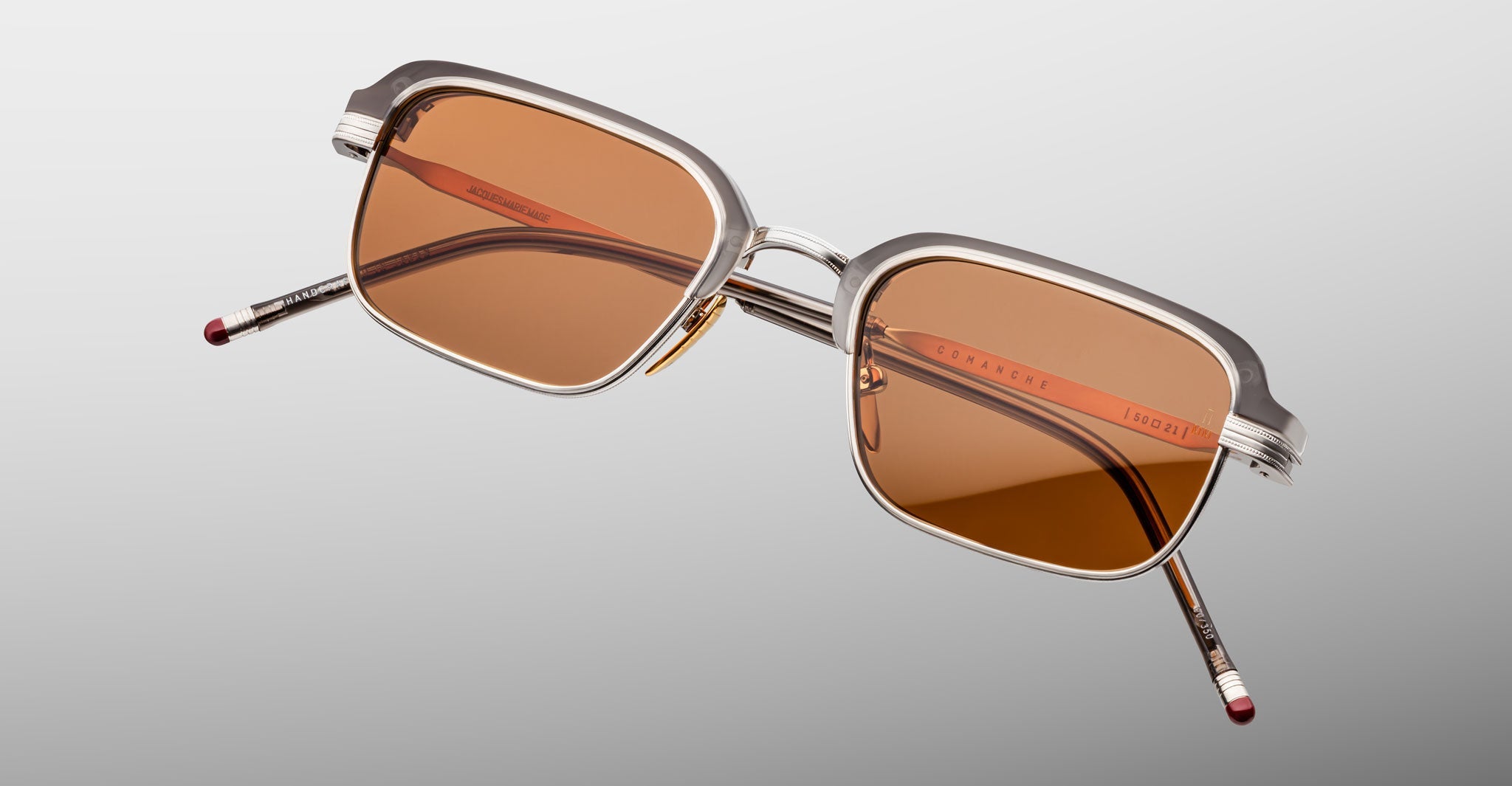 The Jacques Marie Mage Comanche sunglasses feature handcrafted transparent frames and rectangular brown tinted lenses, set against a light gray background—a striking limited-edition eyewear piece by Jacques Marie Mage.