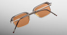 The Jacques Marie Mage Comanche sunglasses, featuring rectangular brown lenses, a silver nose bridge, and transparent frames, are displayed from the back against a light gray background.