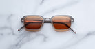 Jacques Marie Mage Comanche in tempest rectangular sunglasses with brown lenses and silver frames, top-down view.
