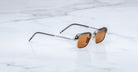 The Jacques Marie Mage Comanche sunglasses, featuring brown lenses and transparent gray frames, rest on a white marble surface—a striking limited-edition piece from Jacques Marie Mage.