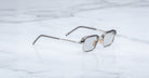 A pair of rectangular, translucent Jacques Marie Mage Comanche eyeglasses with thin arms rests on a white marble surface—a limited-edition design from Jacques Marie Mage.