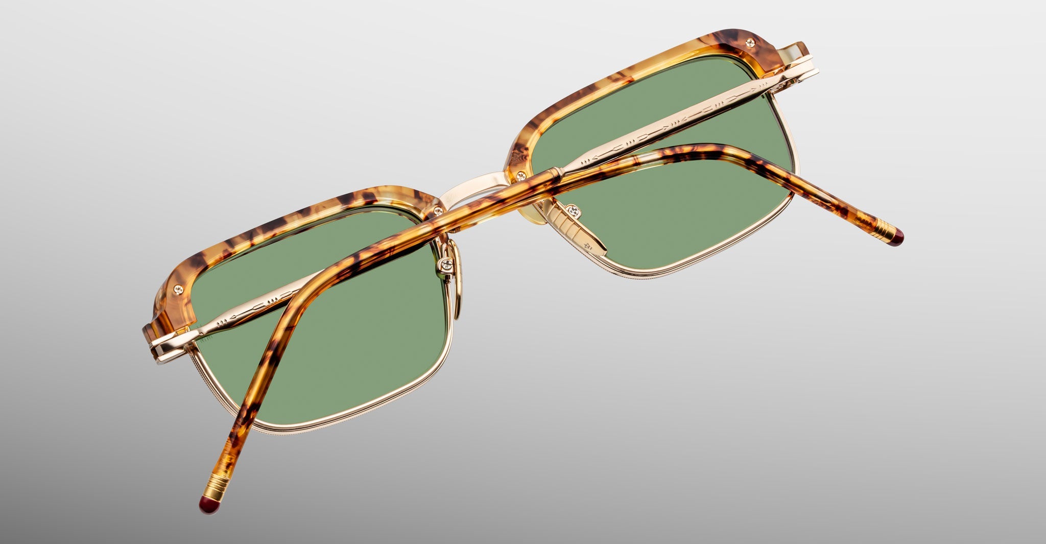 A pair of limited-edition Jacques Marie Mage Comanche rectangular tortoiseshell eyeglasses with green lenses is displayed from the rear on a light gray background, highlighting the brand’s distinctive style.