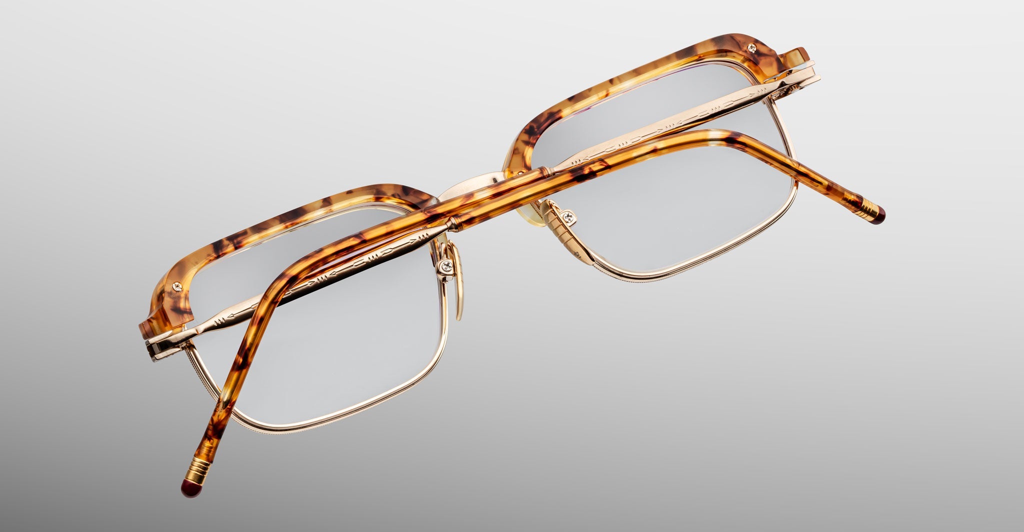 The Jacques Marie Mage Comanche features rectangular tortoiseshell acetate frames and gold metal temples, shown from above on a gradient gray background—a striking limited-edition eyewear choice from Jacques Marie Mage.