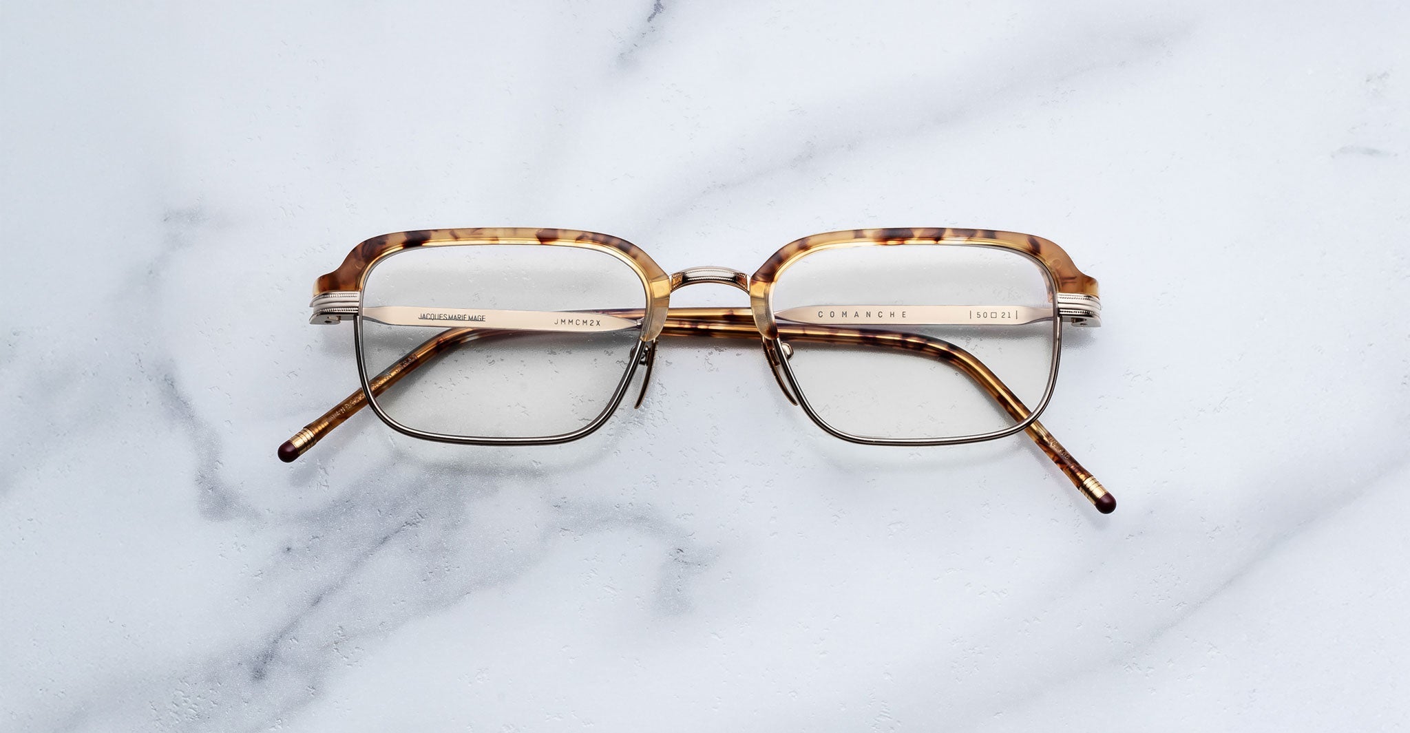 The Jacques Marie Mage Comanche is a pair of rectangular tortoiseshell eyeglasses with gold accents, displayed on white marble—a stunning limited-edition piece from Jacques Marie Mage.