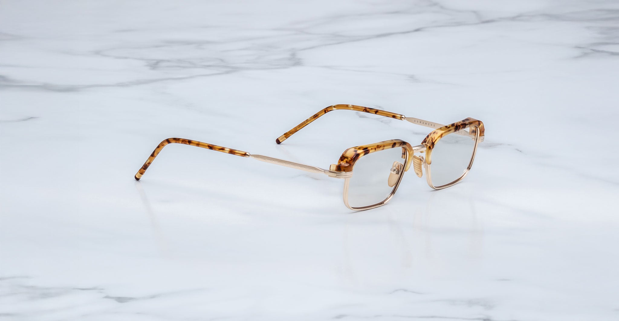 The Jacques Marie Mage Comanche rectangular tortoiseshell eyeglasses, known for their thin frames and limited-edition design, rest on a white marble surface.