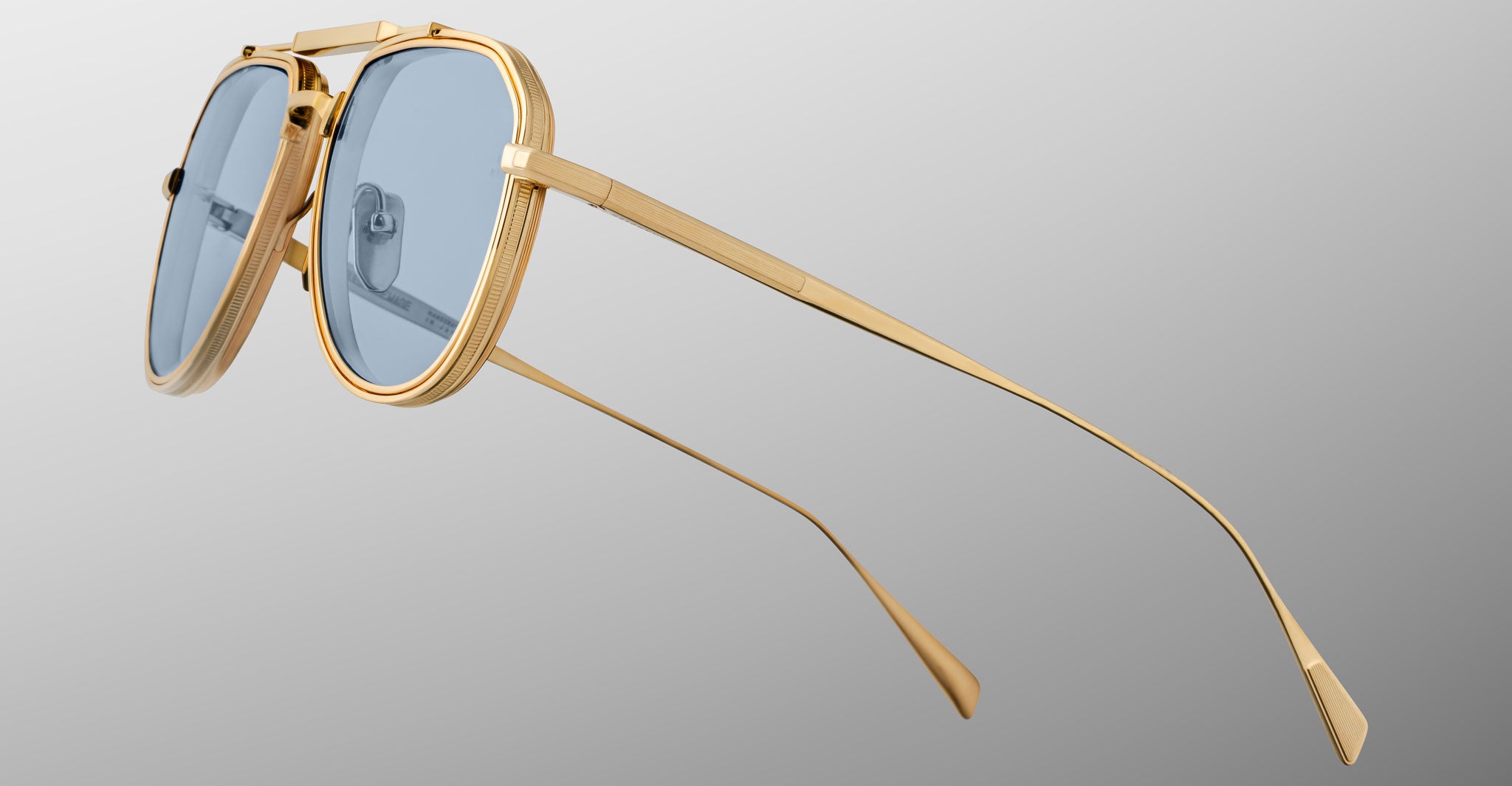 The Jacques Marie Mage Commander sunglasses, featuring gold frames, blue-tinted lenses, thin arms, and a double bridge design, are displayed in close-up against a light gray background.