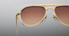 Close-up of the right side of Jacques Marie Mage Commander gold-framed aviator sunglasses with brown gradient lenses against a plain, light gray background.