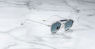 Profile view of the Jacques Marie Mage Dasan titanium sunglass in silver with blue gradient lenses on a white marbled with grey veining background