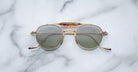 Front view of the Jacques Marie Mage Dasan titanium sunglass in gold color with light grey lenses on a white marbled with grey veining background
