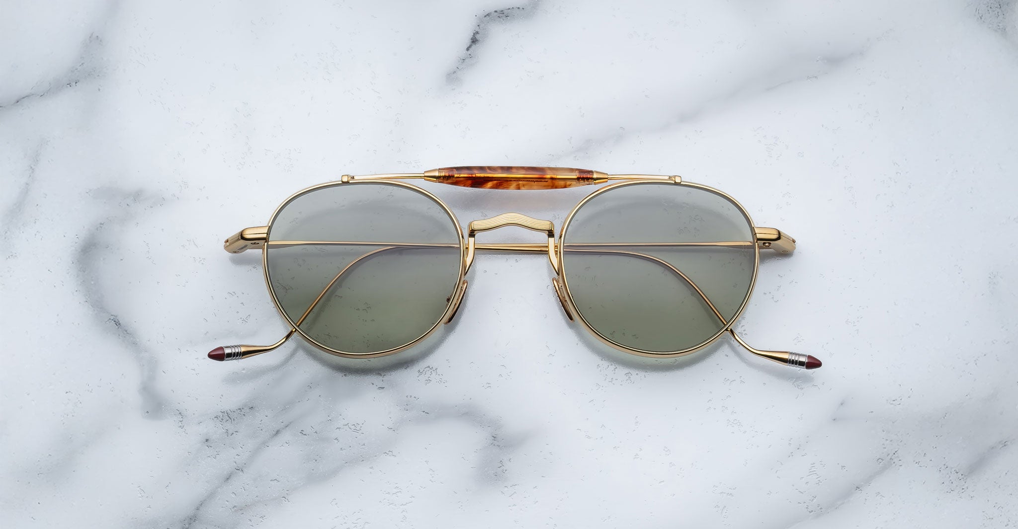 Front view of the Jacques Marie Mage Dasan titanium sunglass in gold color with light grey lenses on a white marbled with grey veining background